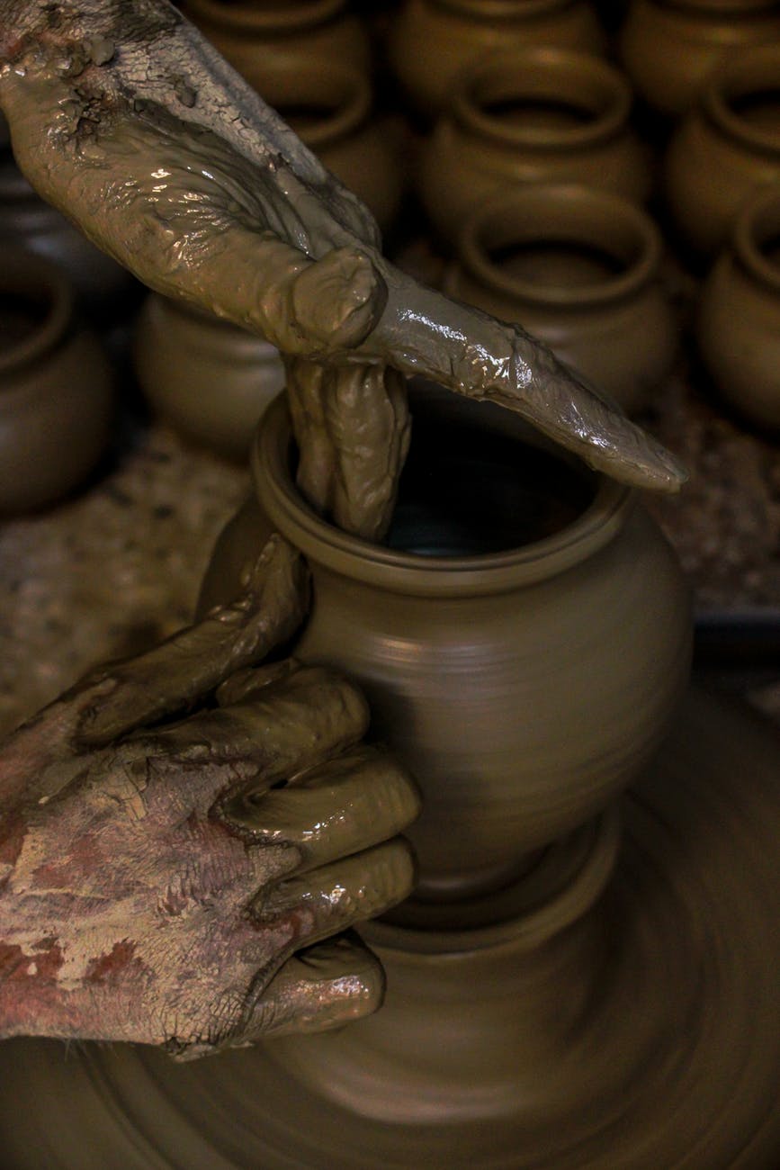 person molding brown clay pot